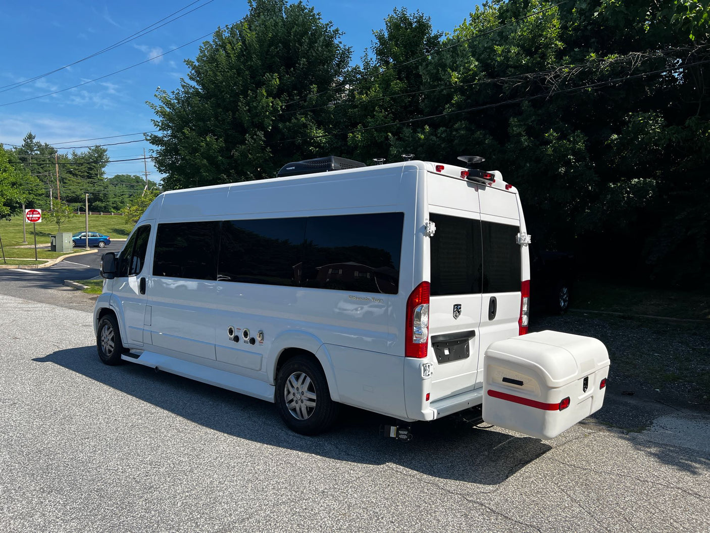 White camper van RV rental, equipped with utility hookups & a rear storage box, parked on asphalt.