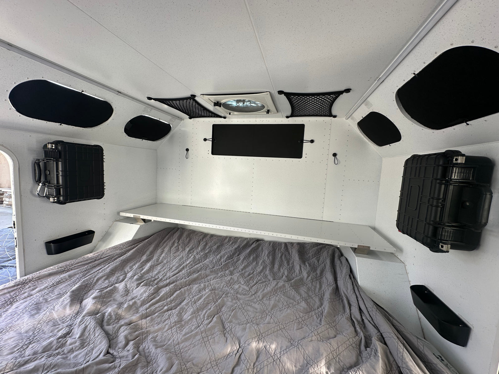 Bright rv rental interior featuring a quilted bed, overhead shelf, wall storage cases, and ceiling fan for comfortable travel.