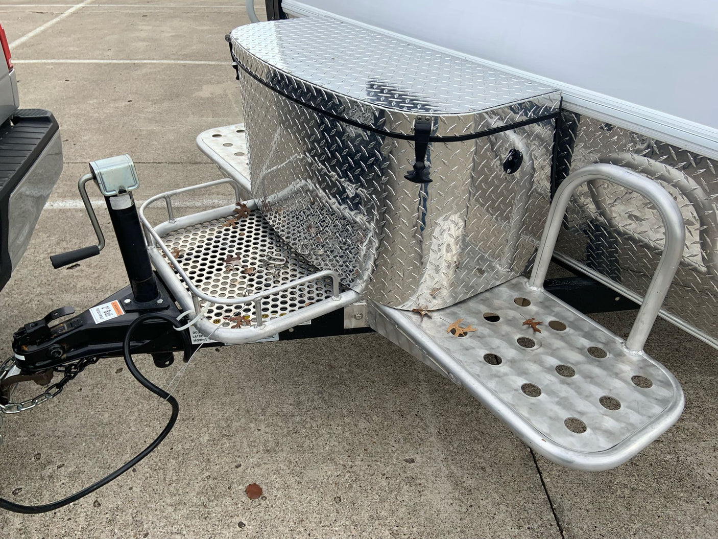 RV rental trailer's front hitch area, featuring a diamond plate storage box, steps, and crank jack.