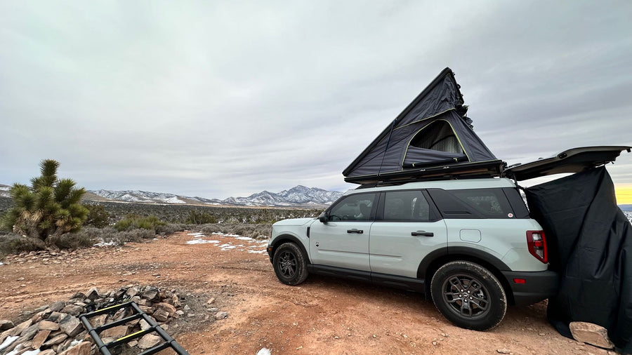 plus a Heytrip gear bag.|Desert camping with an RV rental: An SUV with a pop-up rooftop tent sits amidst mountains. People relax