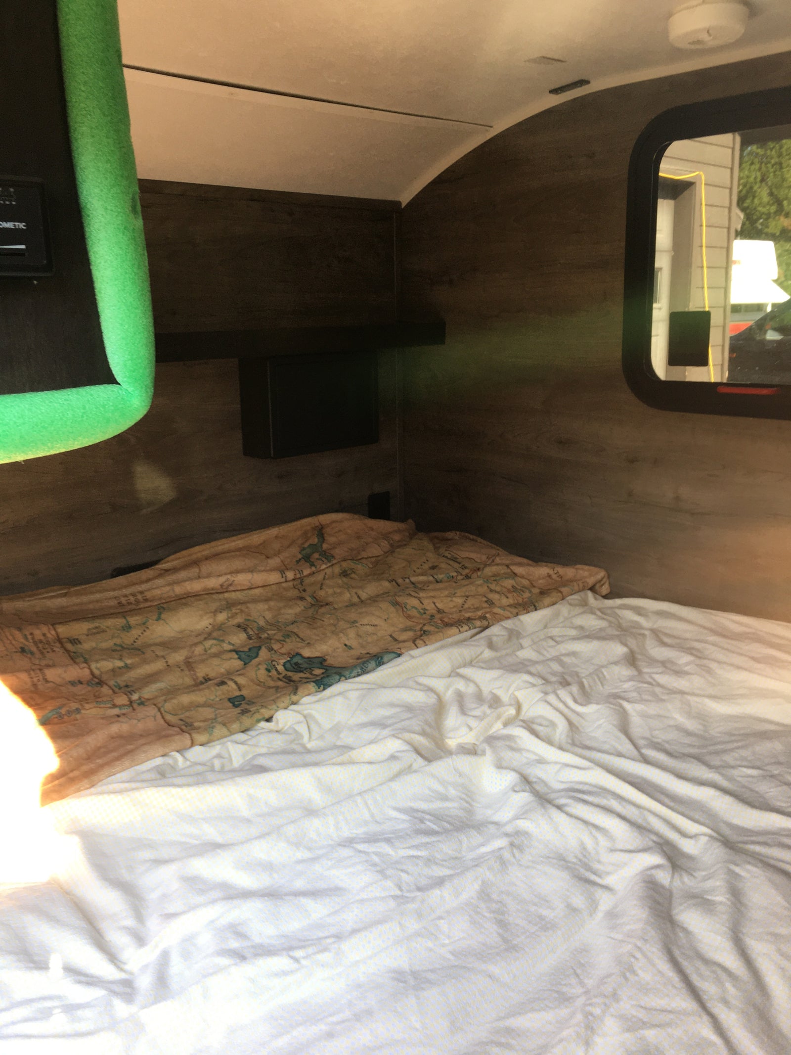 An rv rental bedroom features a cozy bed with a map blanket, white sheets, and warm wooden interior walls.