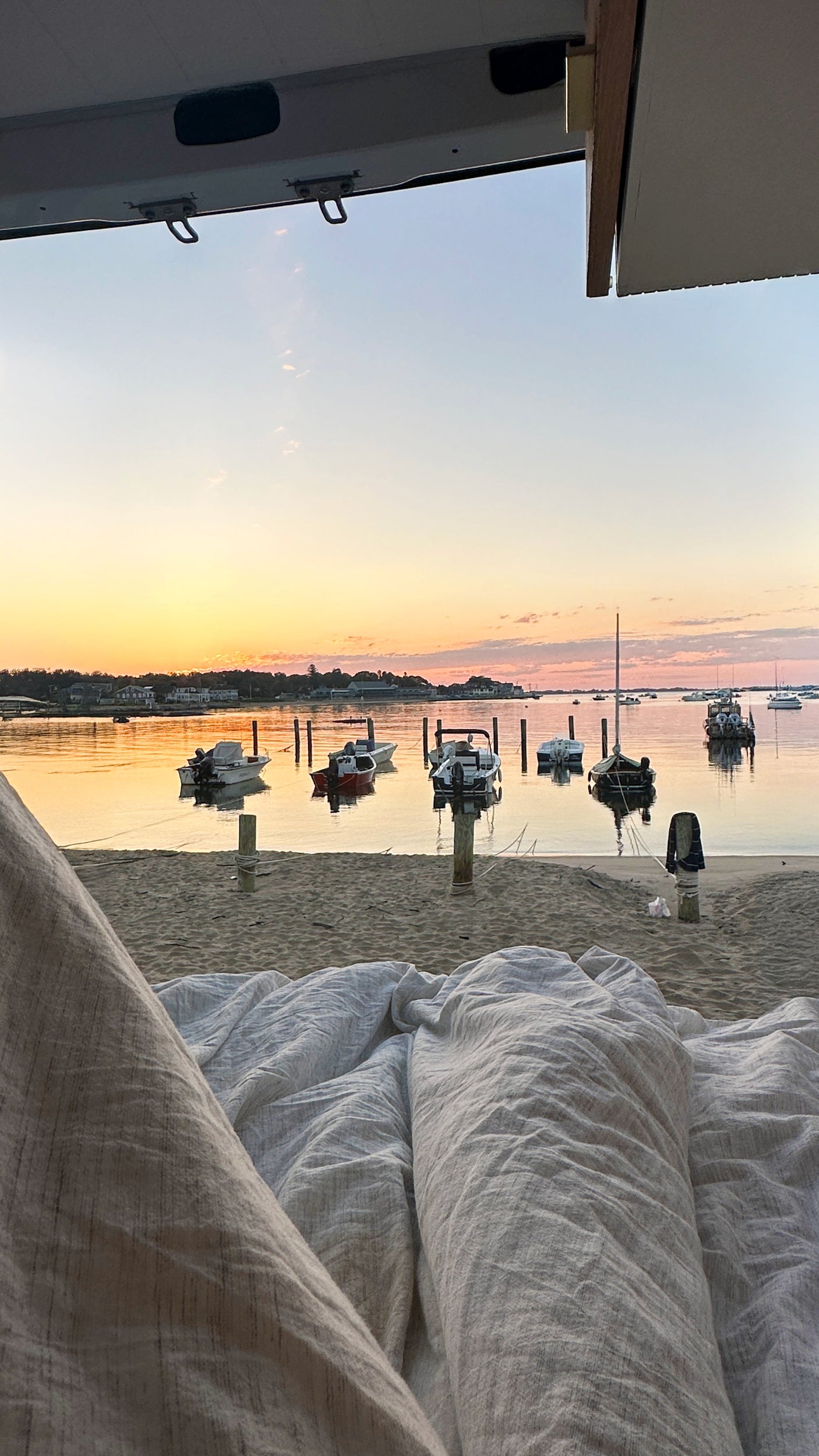 Relaxing inside an RV rental, watching a beautiful sunset over a beach and bay filled with boats. Peaceful van life.