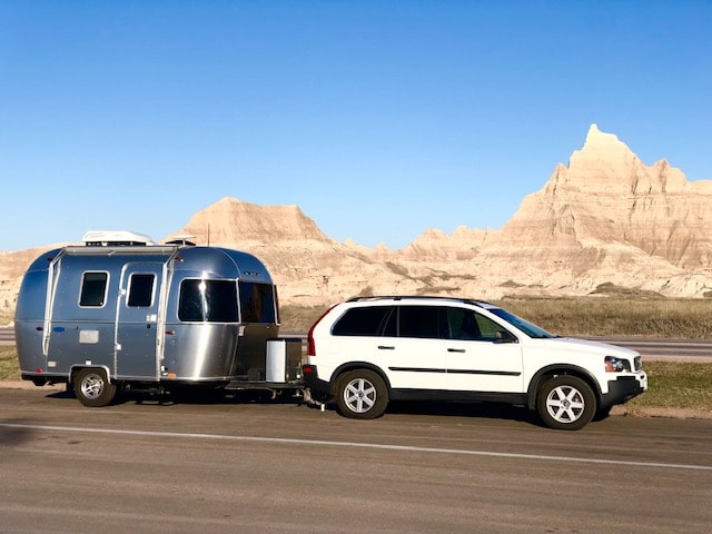 RV rental: A sleek Airstream trailer towed by a white Volvo SUV, set against the striking Badlands formations.