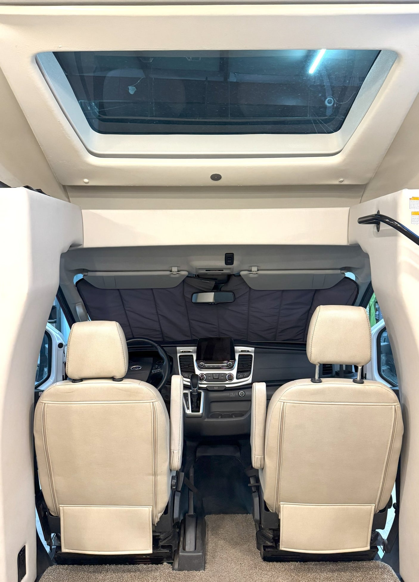 Forward view inside an RV rental showing light-colored front seats, dashboard, and a sunshade. A large skylight is above.