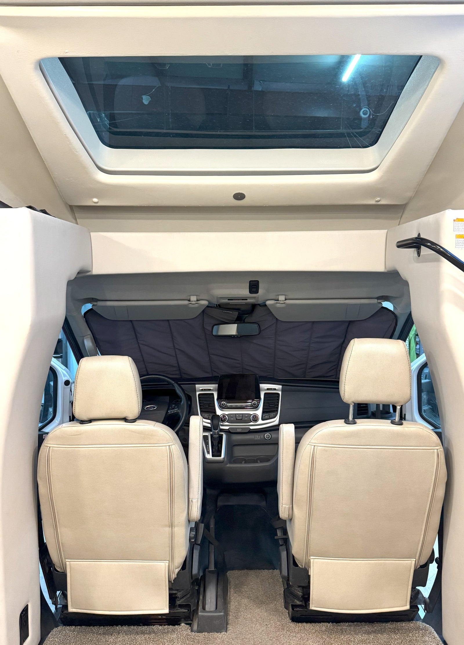 Forward view inside an RV rental showing light-colored front seats, dashboard, and a sunshade. A large skylight is above.