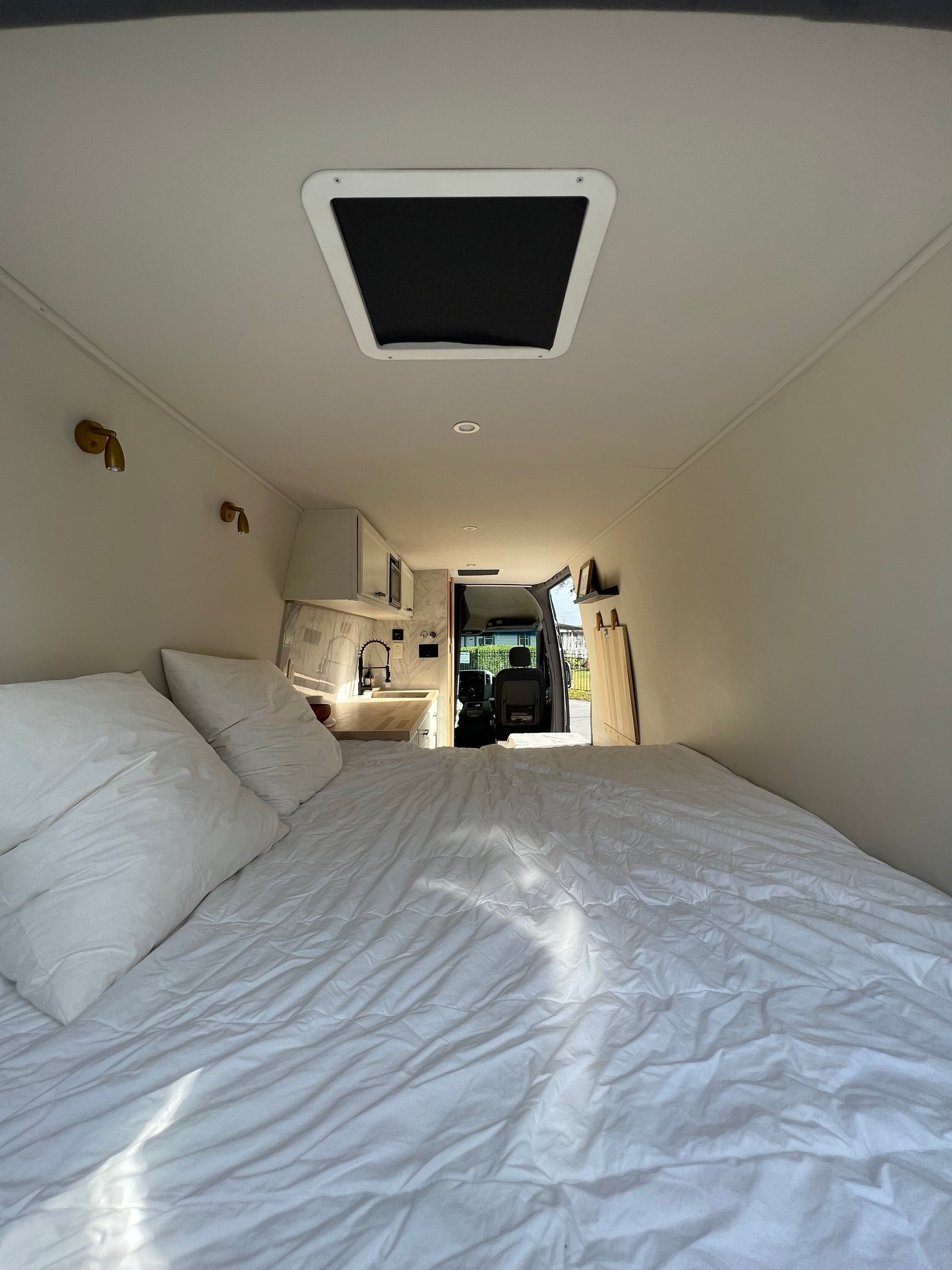 Inside a comfortable RV rental: white bedding, compact kitchen, and open driver's cabin. Ready for the road.