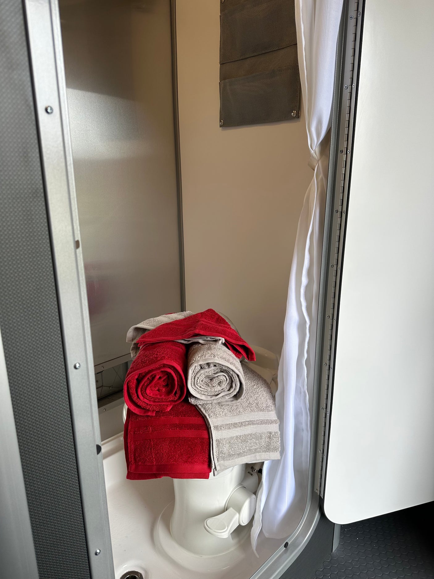RV rental compact bathroom: white toilet with red and gray towels, a shower curtain, and organizational pockets.