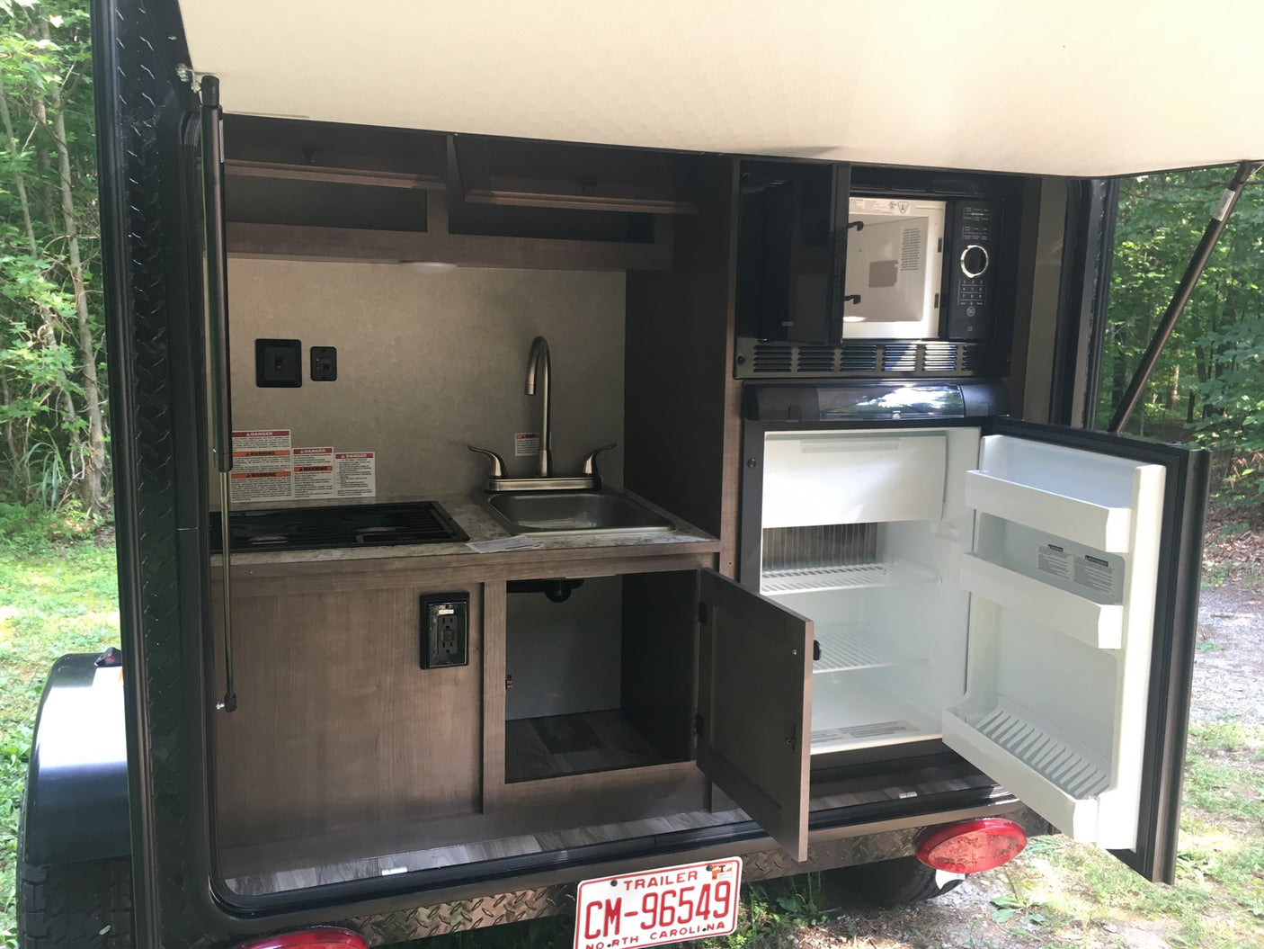 RV rental's compact outdoor kitchen: sink, stove, microwave, and fridge open for use, perfect for camping.