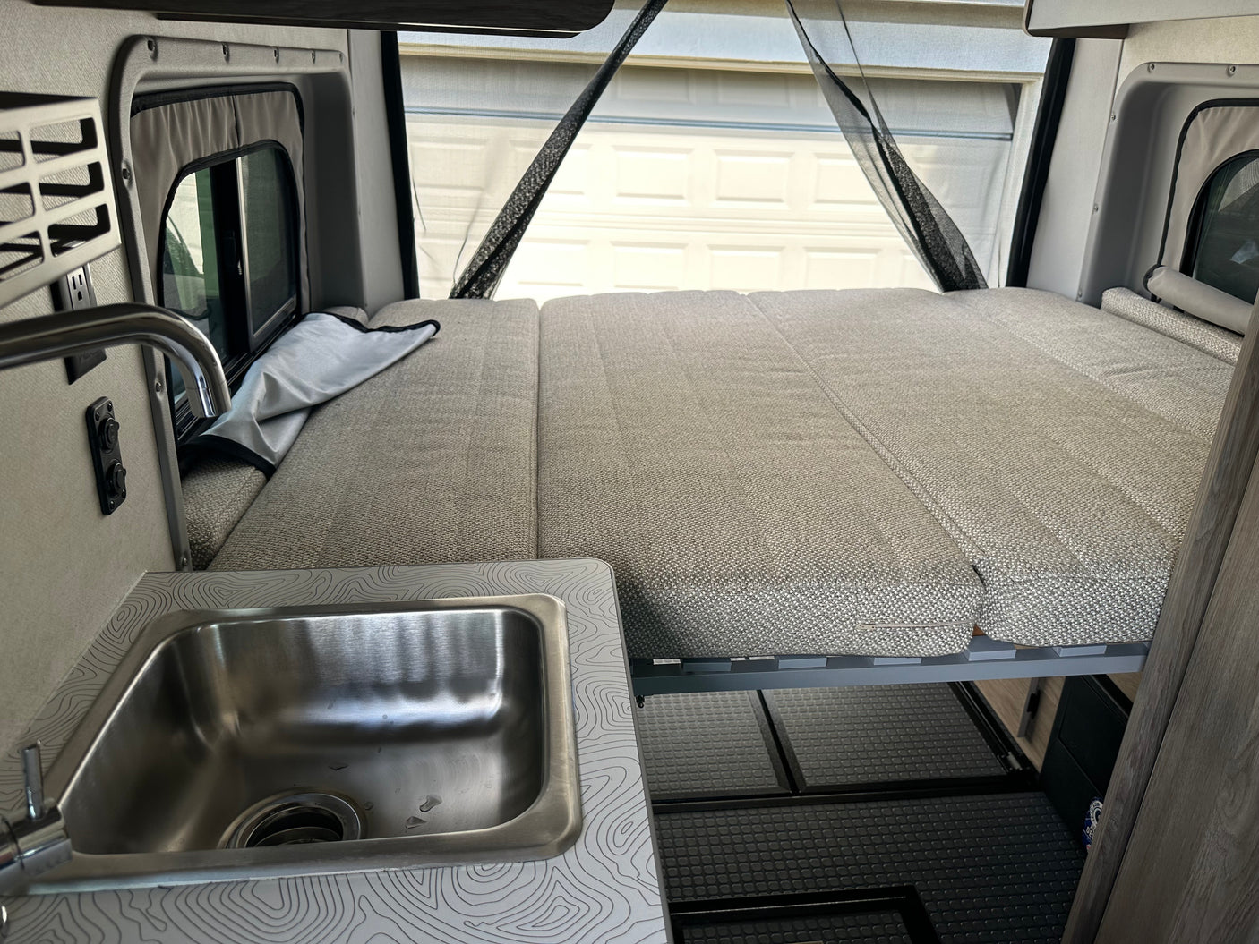 Explore a comfortable RV rental! Features a spacious bed, functional kitchen sink, and clever storage solutions.