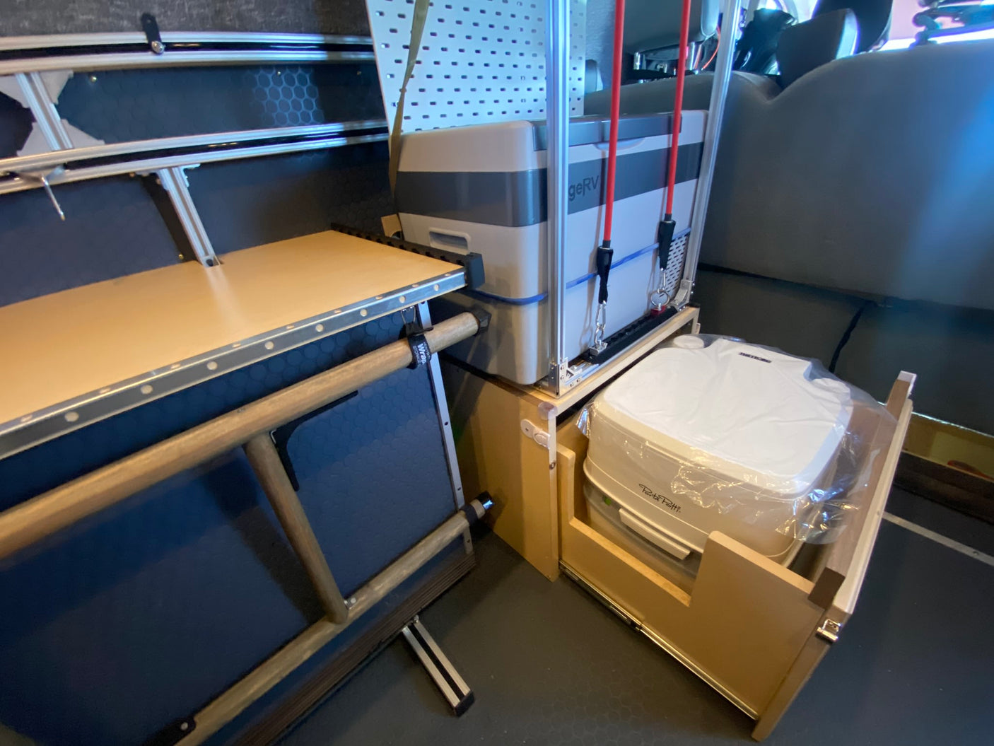 RV rental interior showing a portable fridge, pull-out toilet, and multi-use counter space for compact travel.