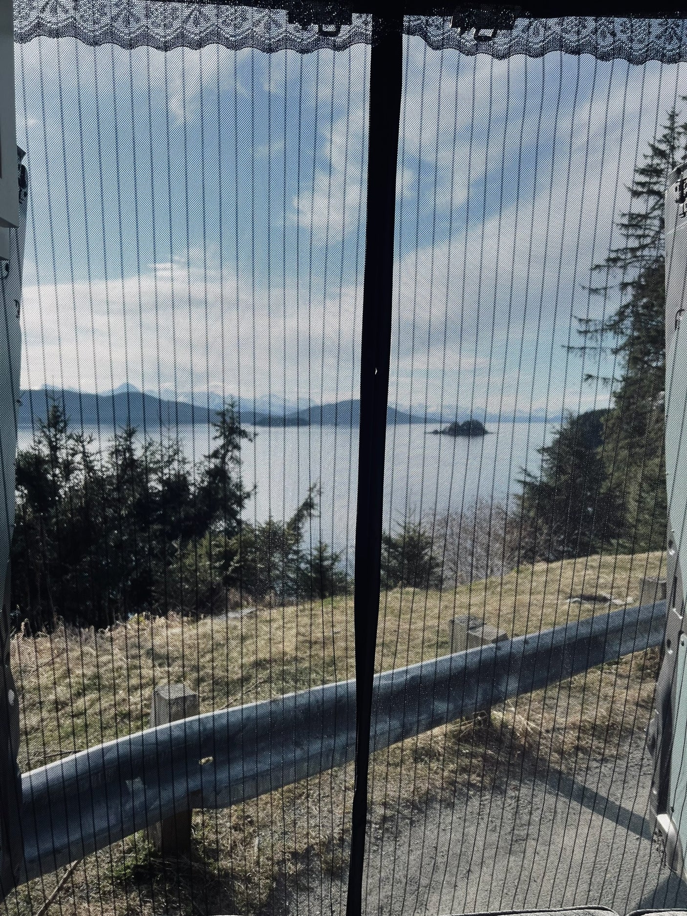 Scenic view from an RV rental: a bay, mountains, and trees, beautifully framed by a mesh screen from inside.