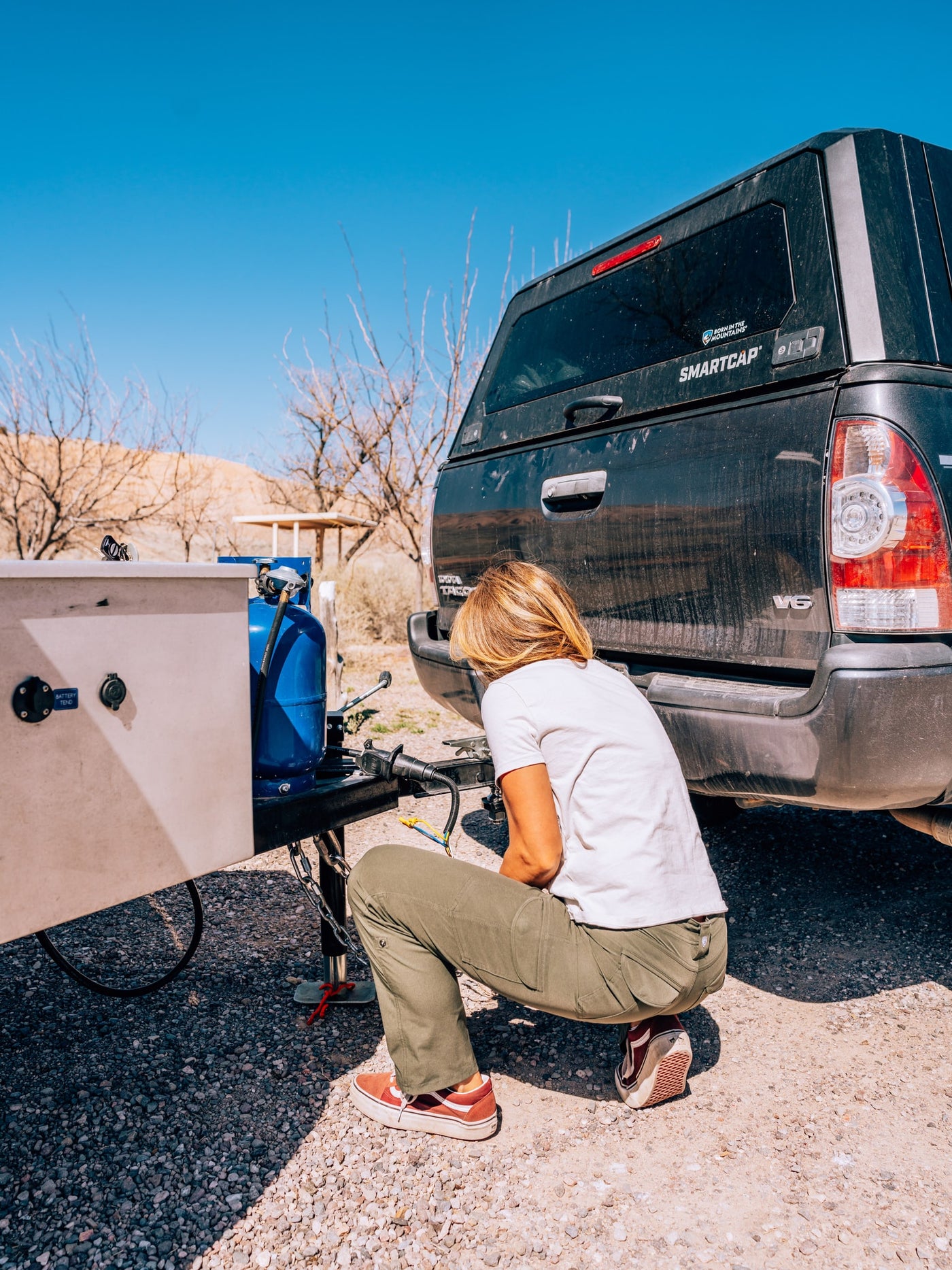 Crouching by an RV rental, a person connects the trailer hitch to a truck, propane tank visible, for outdoor adventure. — photo 9