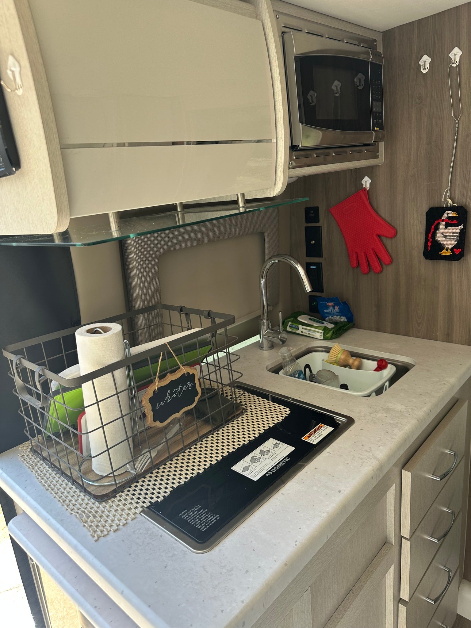 Inside an RV rental: a compact, organized kitchen featuring a sink, covered stove, microwave, and thoughtful storage solutions.