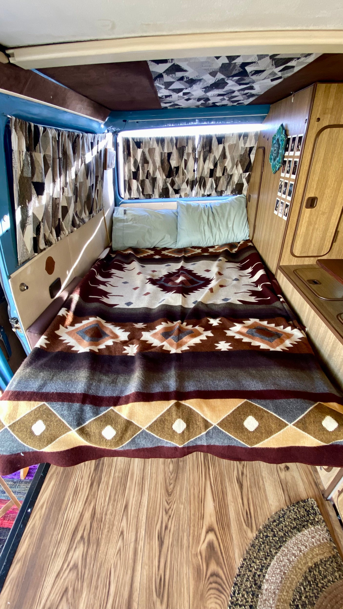 Cozy RV rental interior showing a bed with a patterned blanket, wood floors, and inviting camper van decor.
