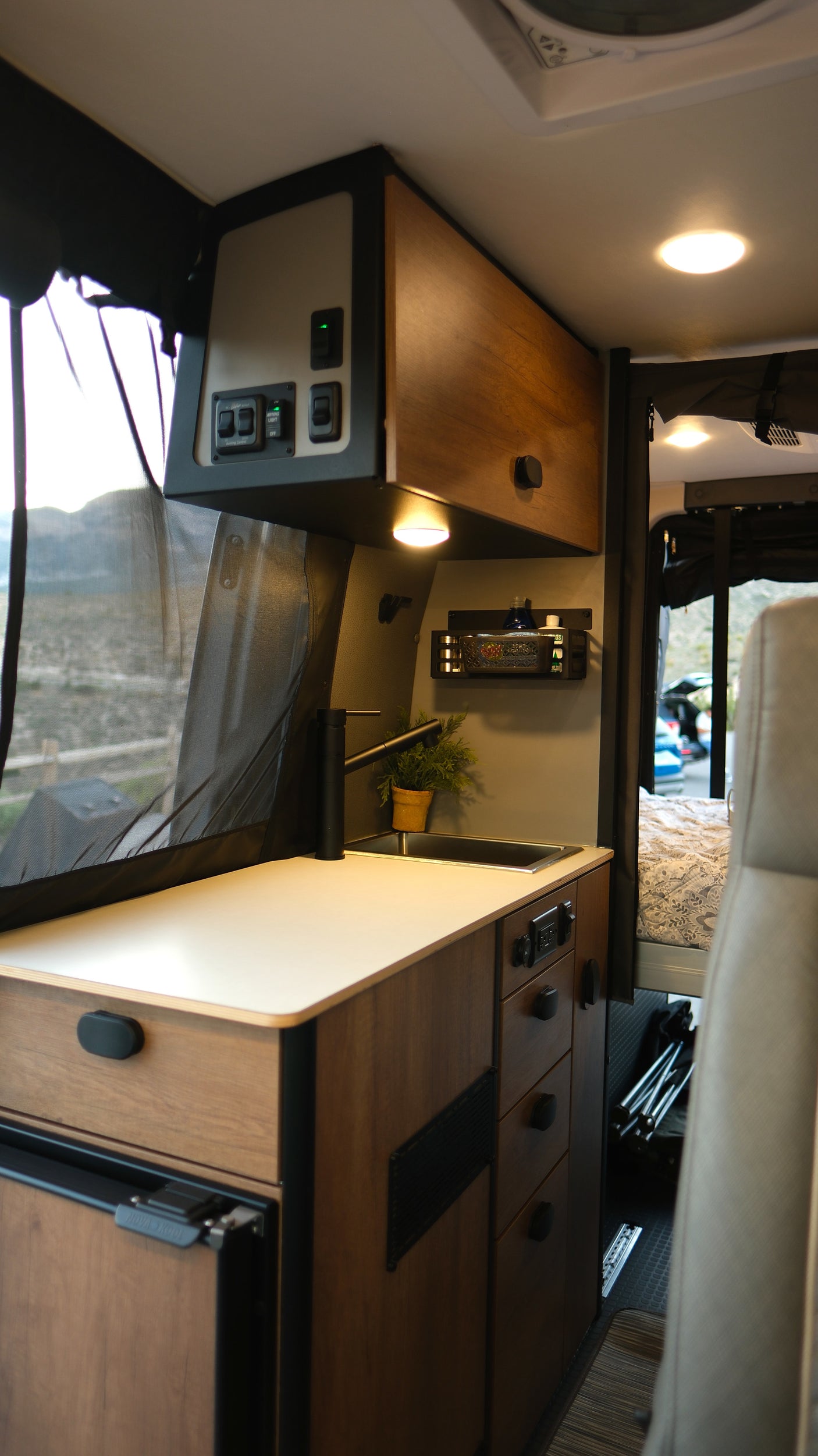 This RV rental's cozy kitchen galley features a sink, fridge, controls, and mountain views through the screen.