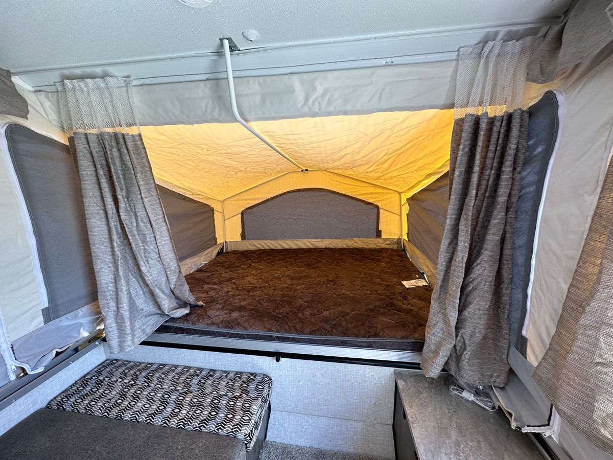 Explore a comfy RV rental pop-up camper bed, with a brown mattress, canvas walls, and patterned seating. — photo 10