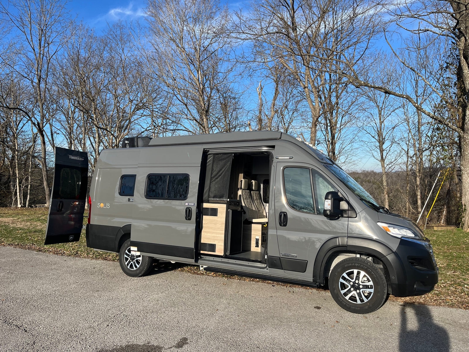 Gray Winnebago Solis camper van for RV rental, parked outdoors with doors open, showcasing its modern interior.