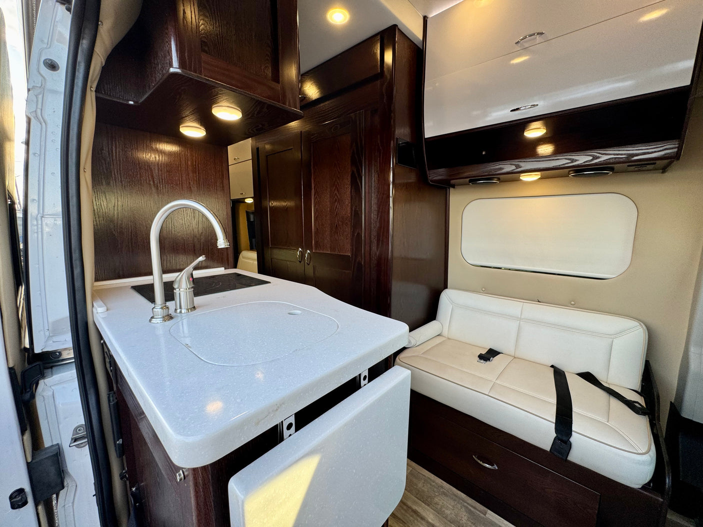 RV rental interior: featuring dark wood cabinetry, a functional kitchen with sink, and a cream bench seat for comfortable travel.
