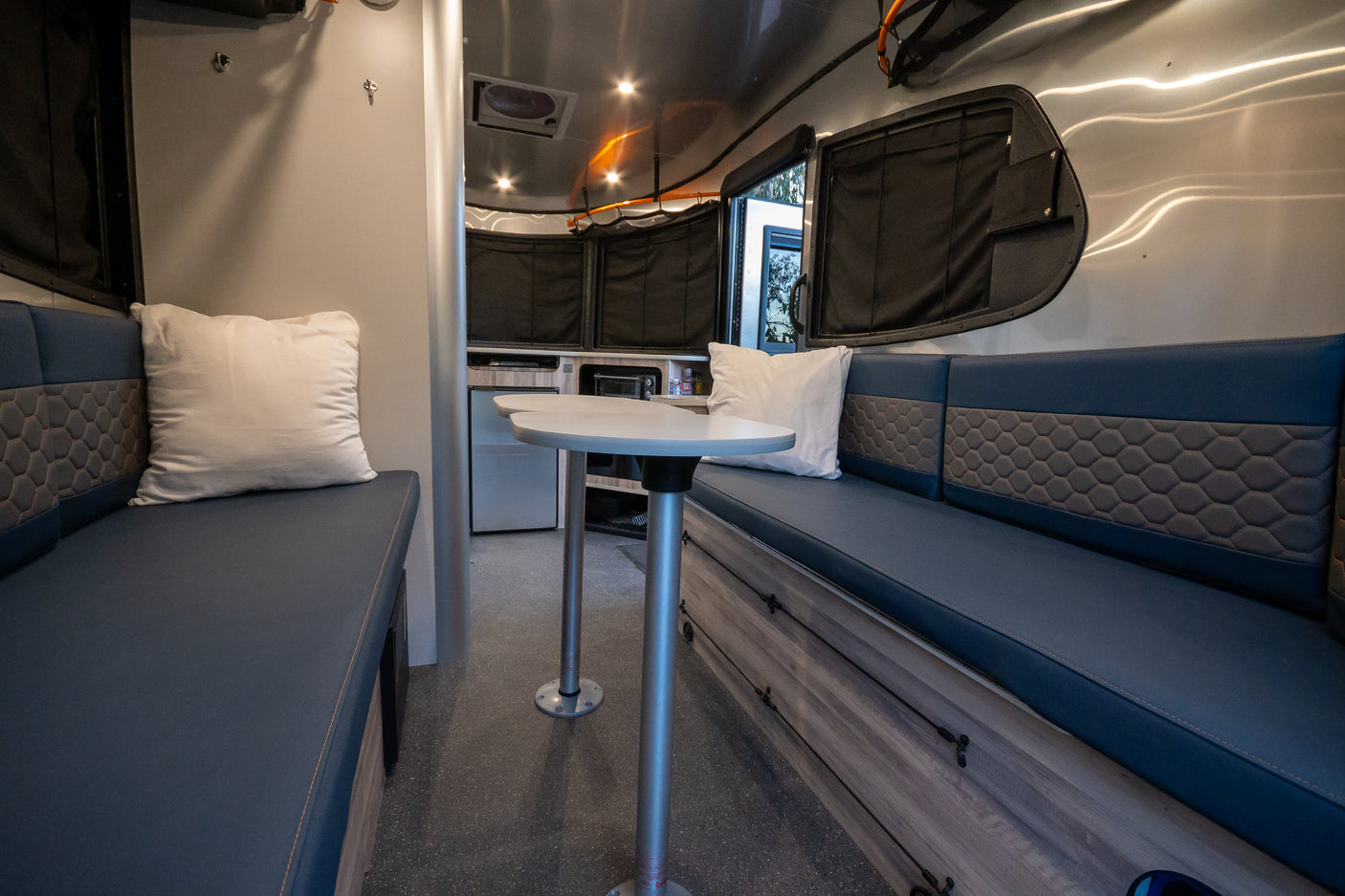 Step inside this modern rv rental, featuring comfortable blue benches, a dining table, and a compact kitchenette area.