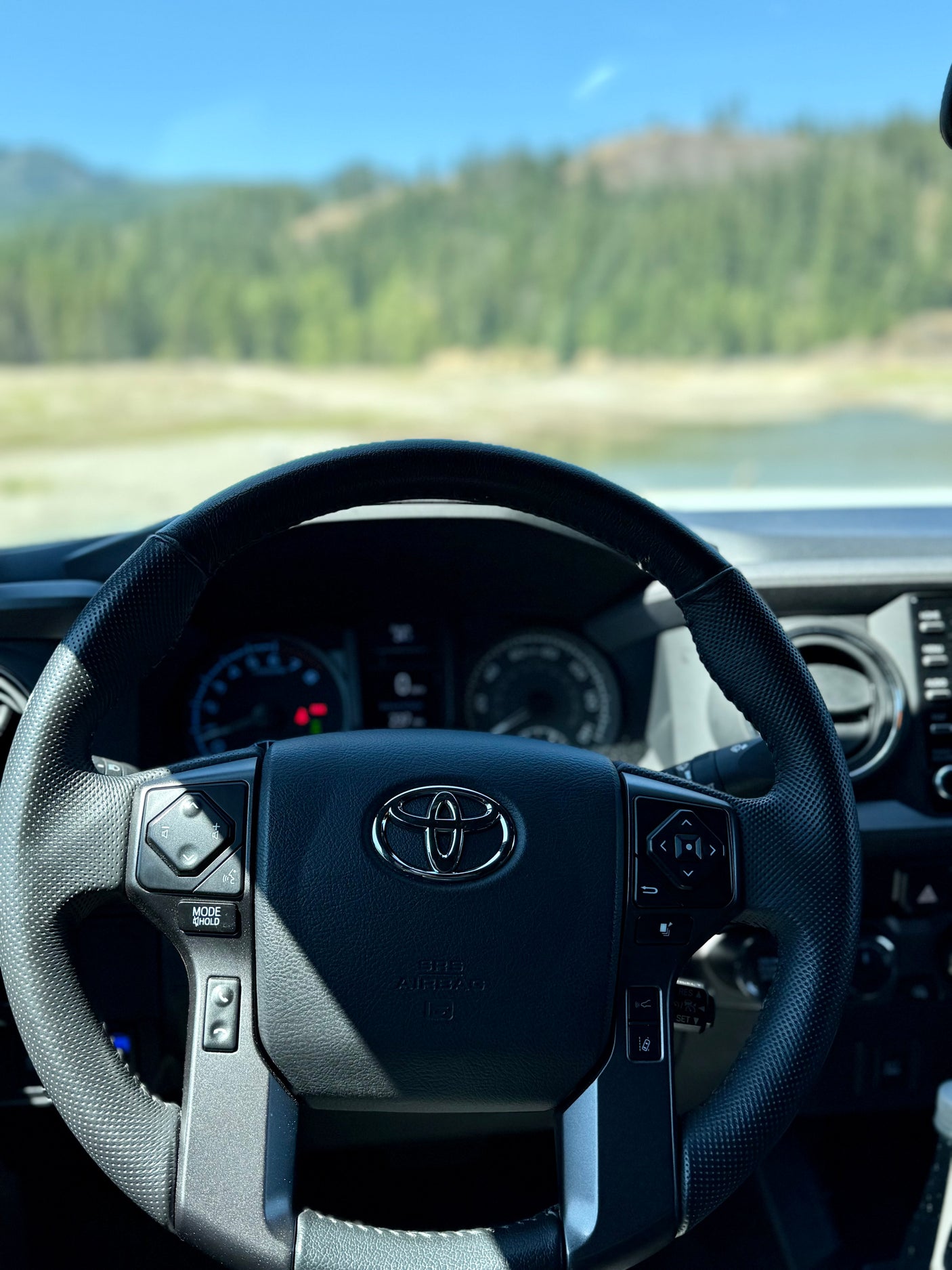 View from a Toyota steering wheel and dashboard overlooking a scenic lake and forest, perfect for an rv rental journey.