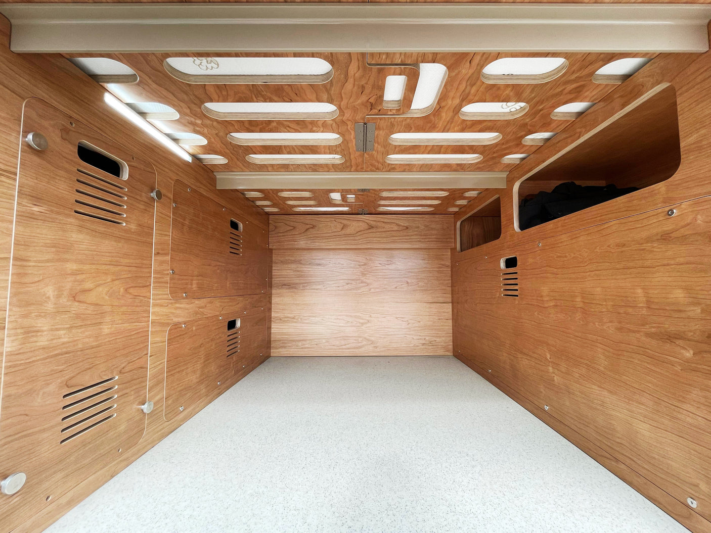 Inside a custom RV rental: wood-paneled interior, built-in storage, patterned ceiling with light strips, and a bright floor.