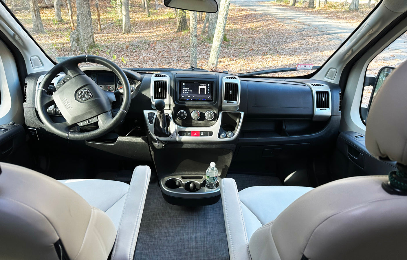 Spacious RV rental interior featuring the dashboard, steering wheel, and front seats, overlooking a forest road.