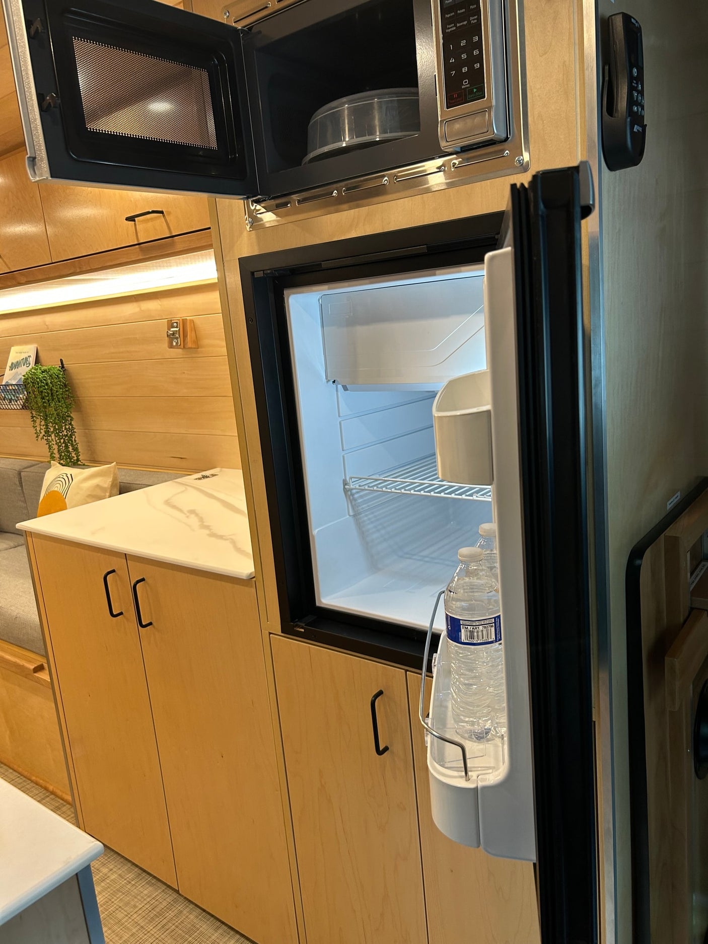 Modern RV rental interior with open microwave, bright refrigerator, and sleek kitchen cabinets.