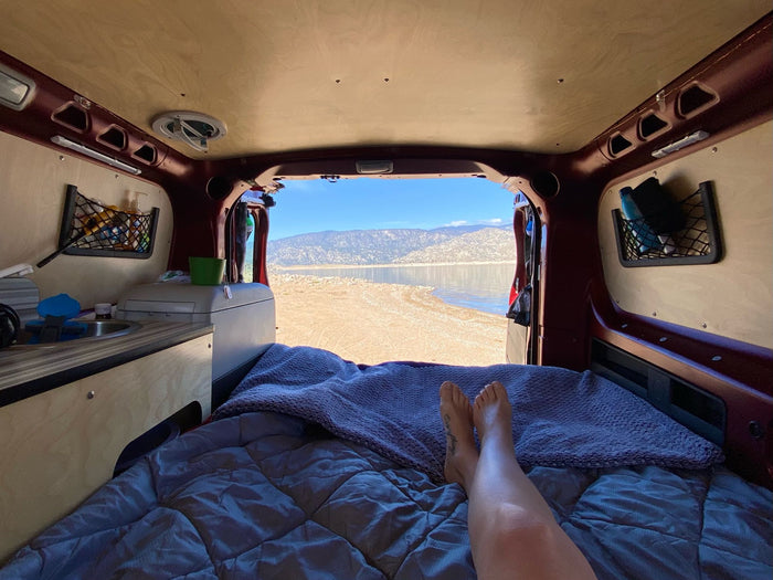 surrounded by mountains.|View from inside a camper van: bare feet on a bed