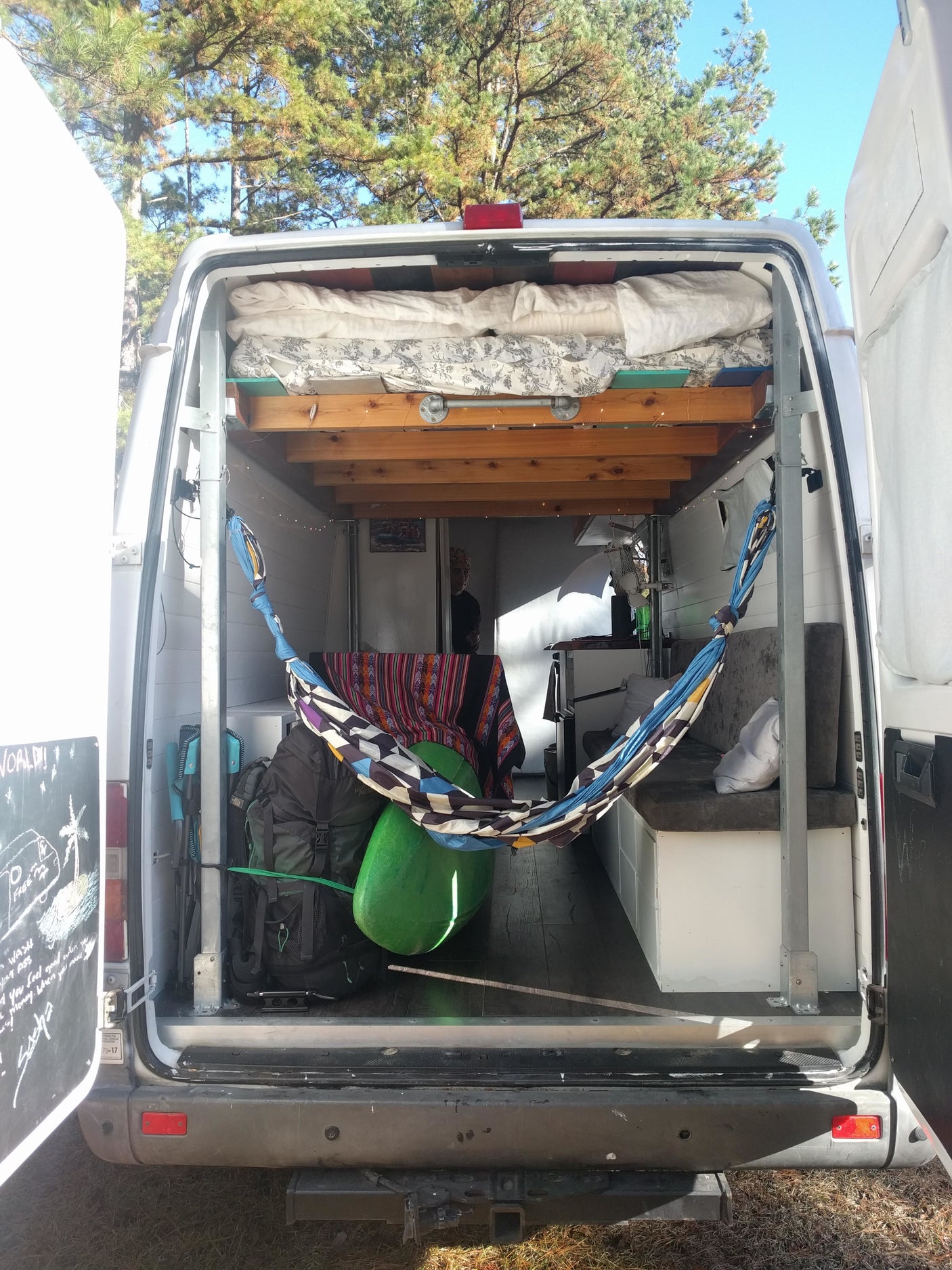 Adventure-ready RV rental interior: elevated bed, hammock, and storage for outdoor gear, offering a compact, cozy van life.