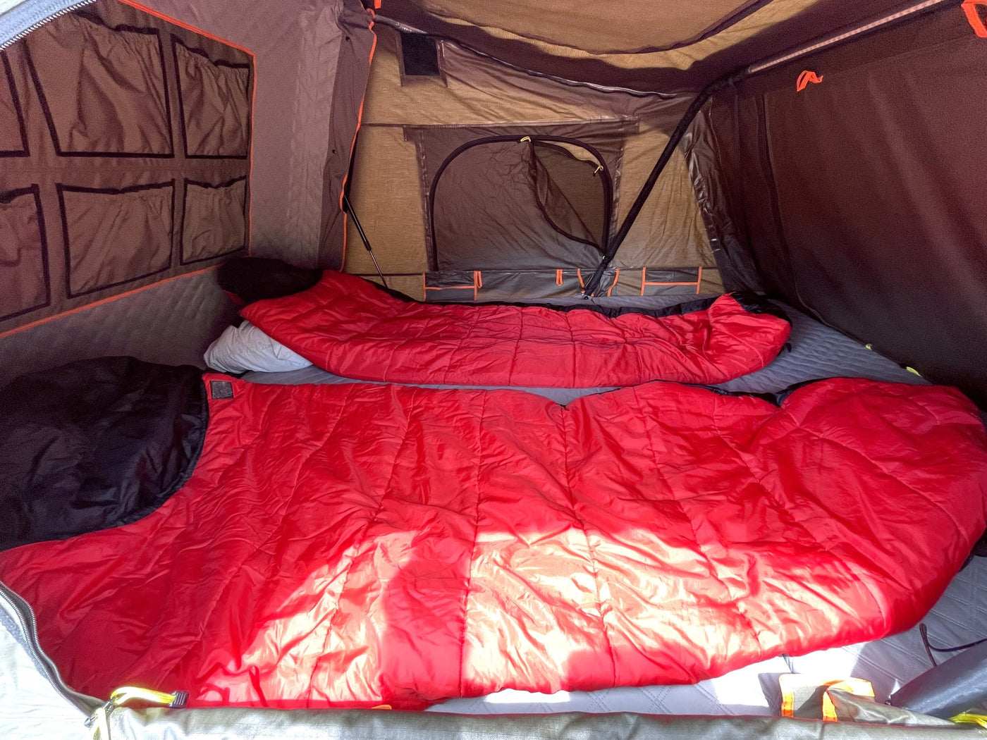 Inside a spacious RV rental tent: two red sleeping bags and pillows are laid out on a mattress, with storage pockets lining the wall. — photo 9