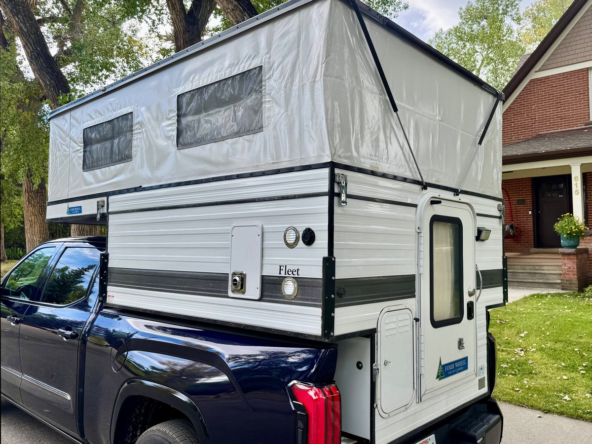 ready for your next RV rental trip.|Night camping with two illuminated RV rentals under a starry blue sky. People gathered outside and inside camper trucks.|A dark blue Toyota Tundra Platinum truck with a white Four Wheel Fleet pop-up camper — photo 2