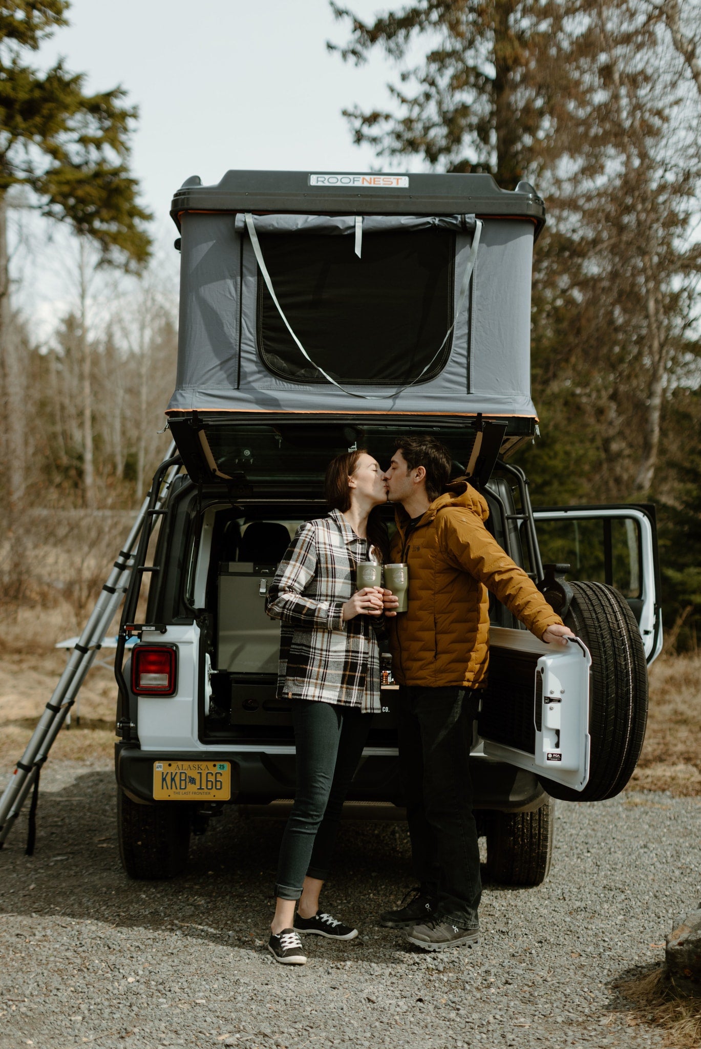 An Alaska RV rental adventure: A couple kisses by their equipped Jeep Wrangler with a Roofnest rooftop tent.