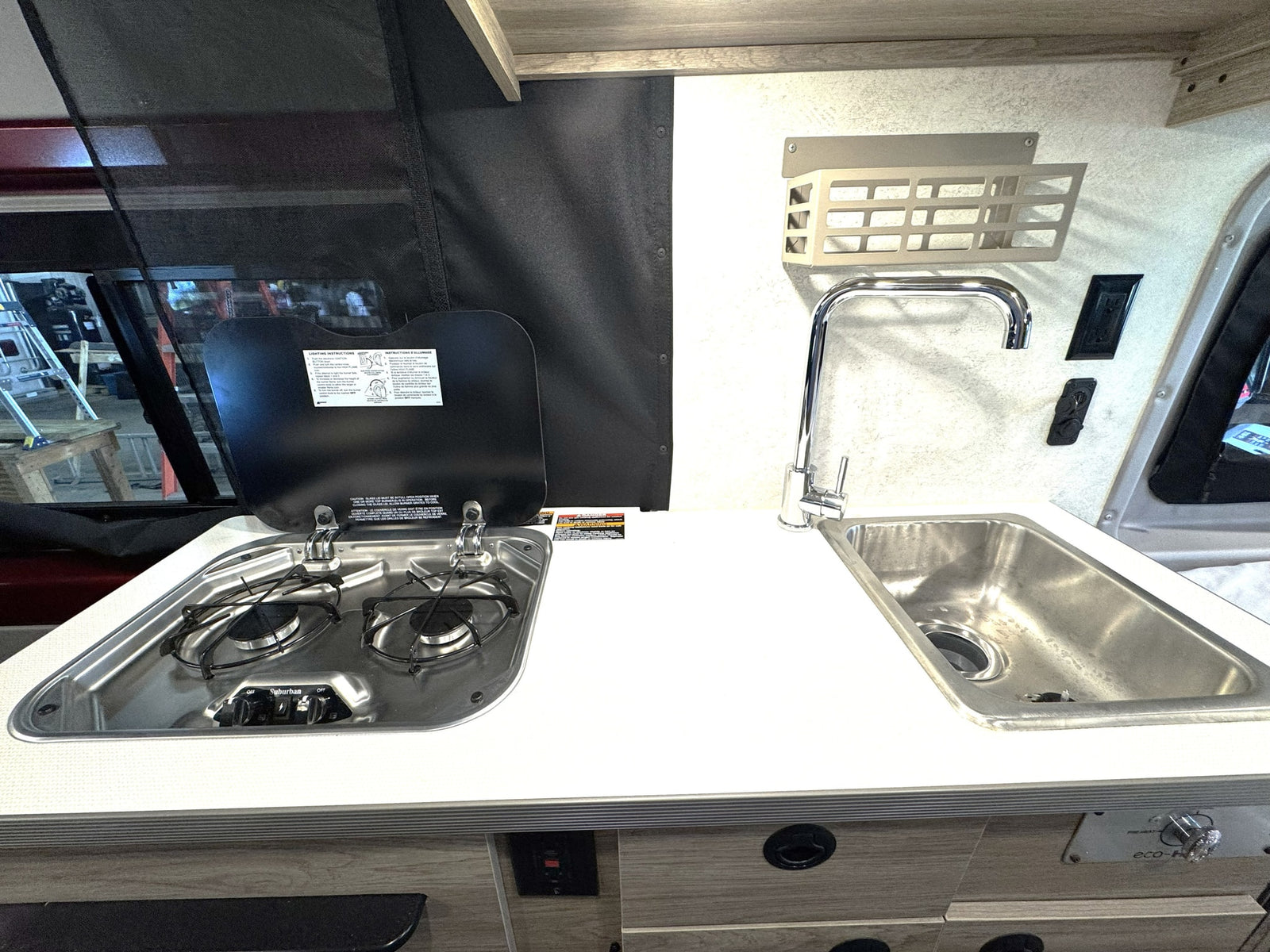 Essential RV rental kitchen setup: a two-burner stove with cover, stainless steel sink, and clean white countertop.