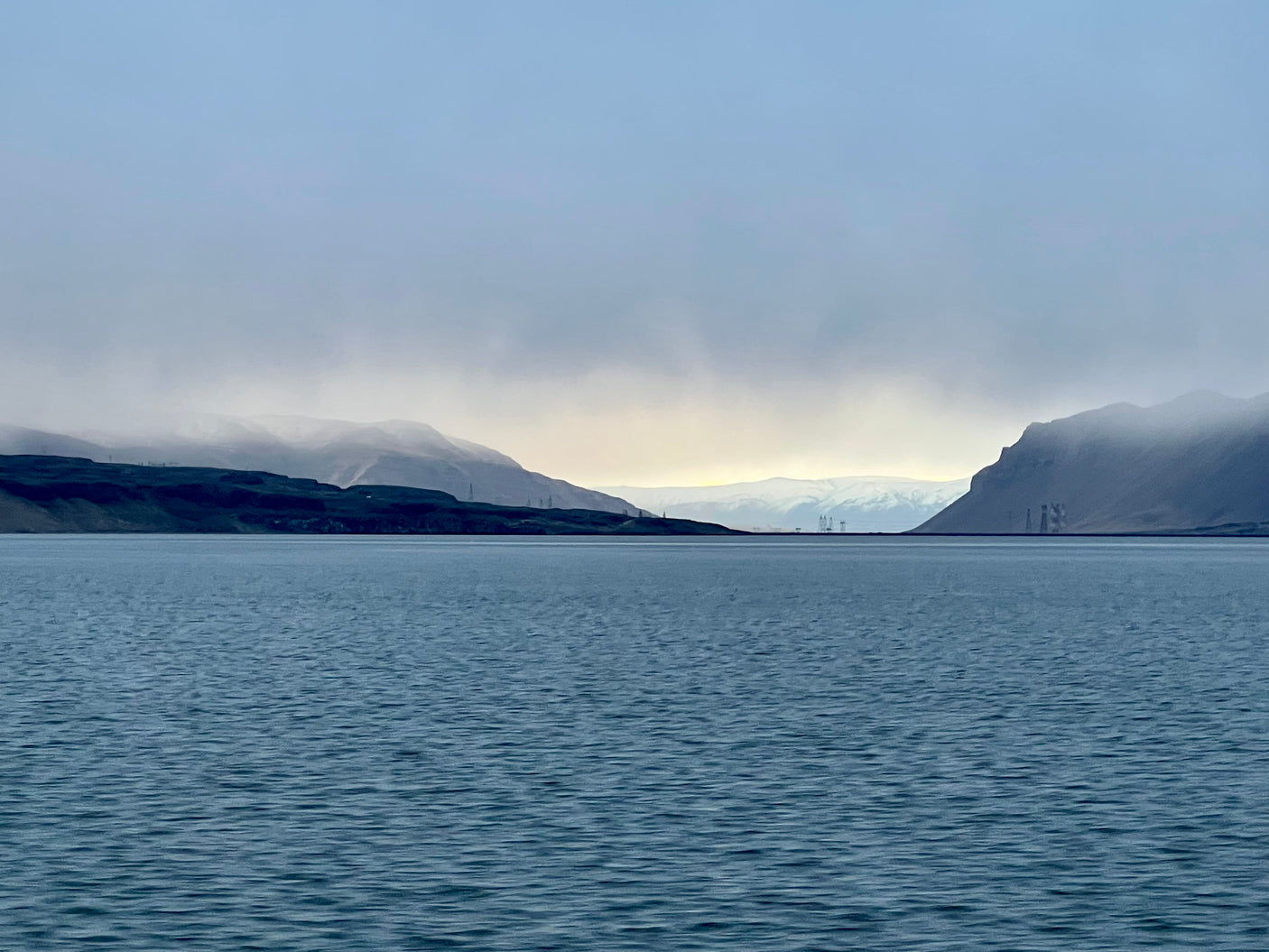 Serene fjord framed by misty mountains under a pale sky. Discover with an RV rental.