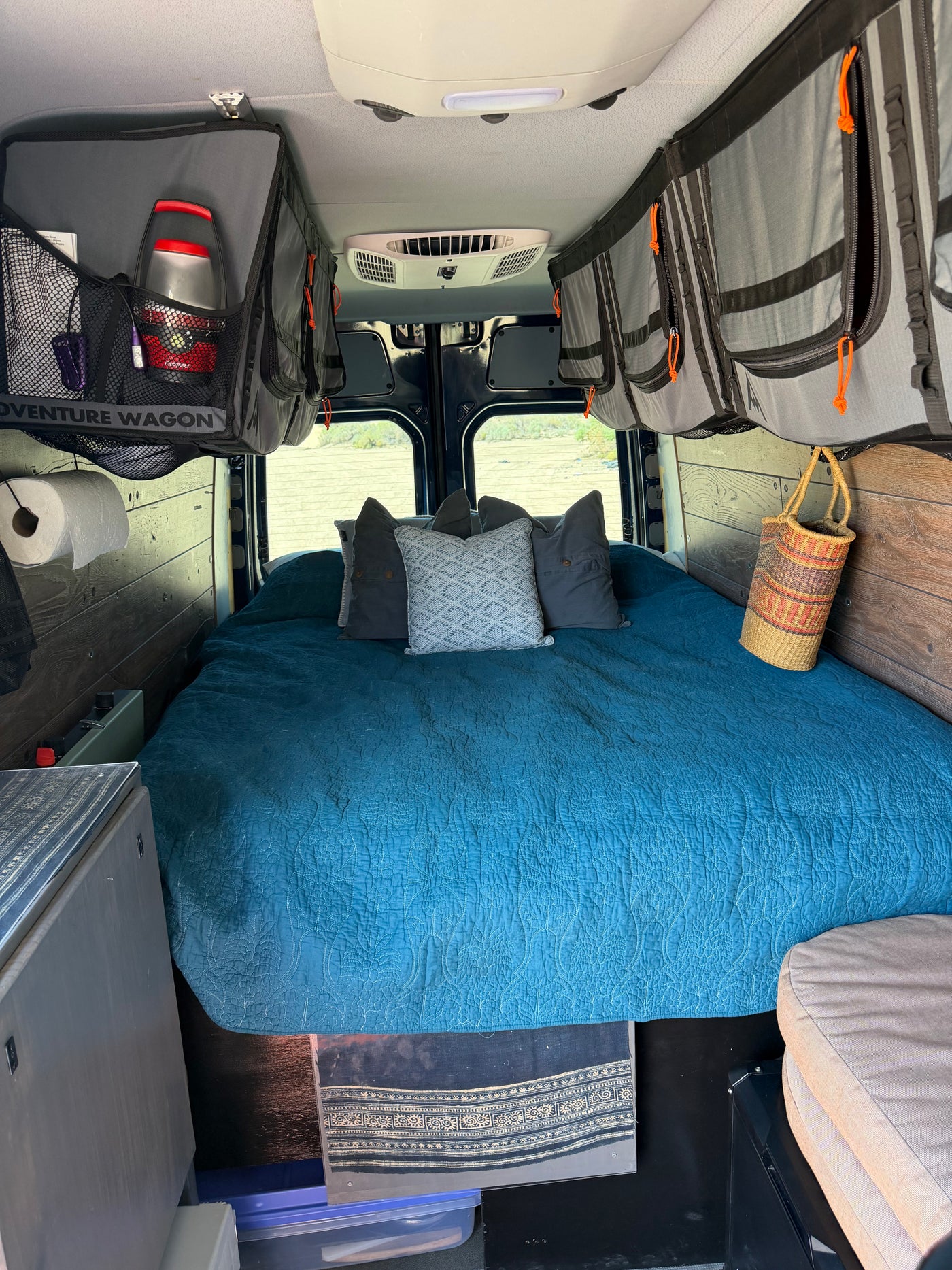 Interior of an **rv rental** featuring a cozy bed with a blue quilt, overhead storage, and rear windows with an outdoor view. — photo 16