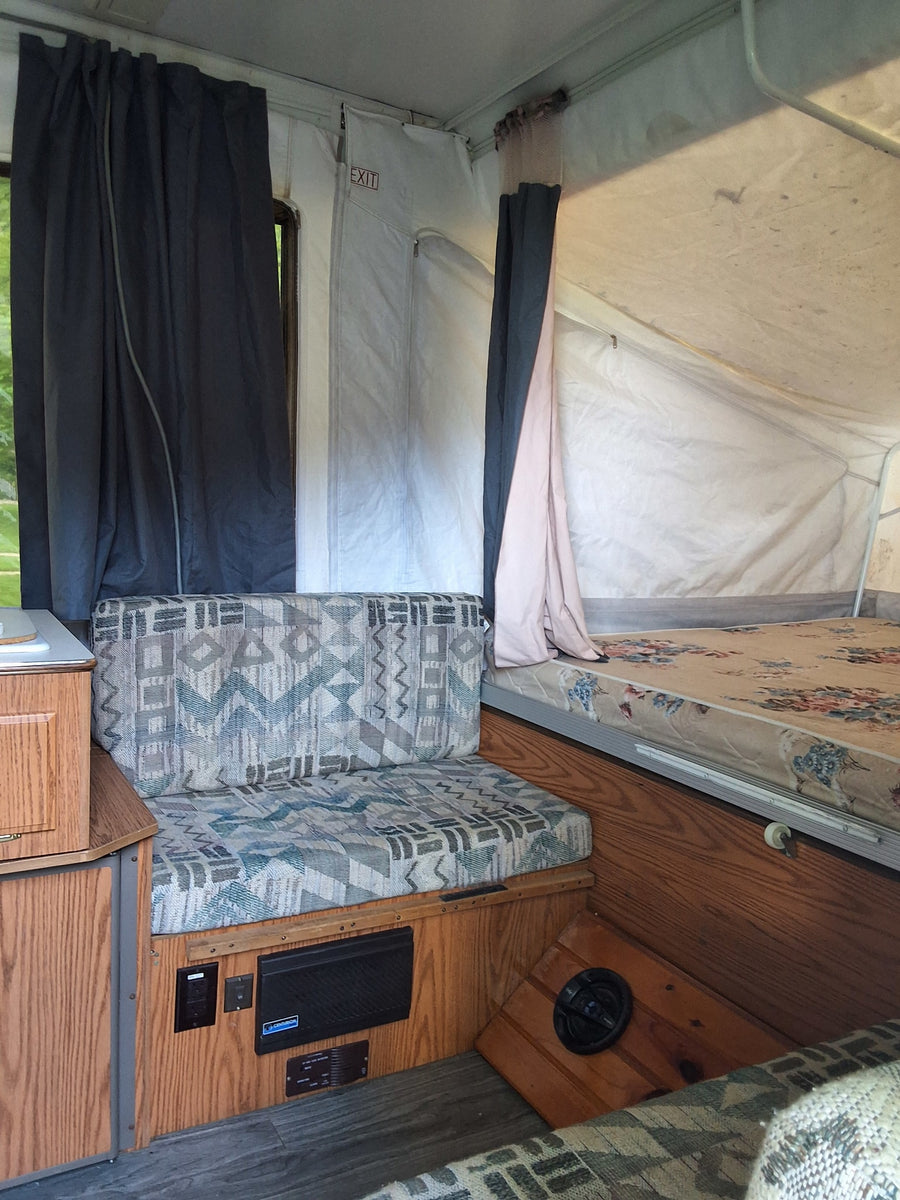 Cozy rv rental interior: pop-up camper with dinette, floral bed, canvas walls, and dark curtains.