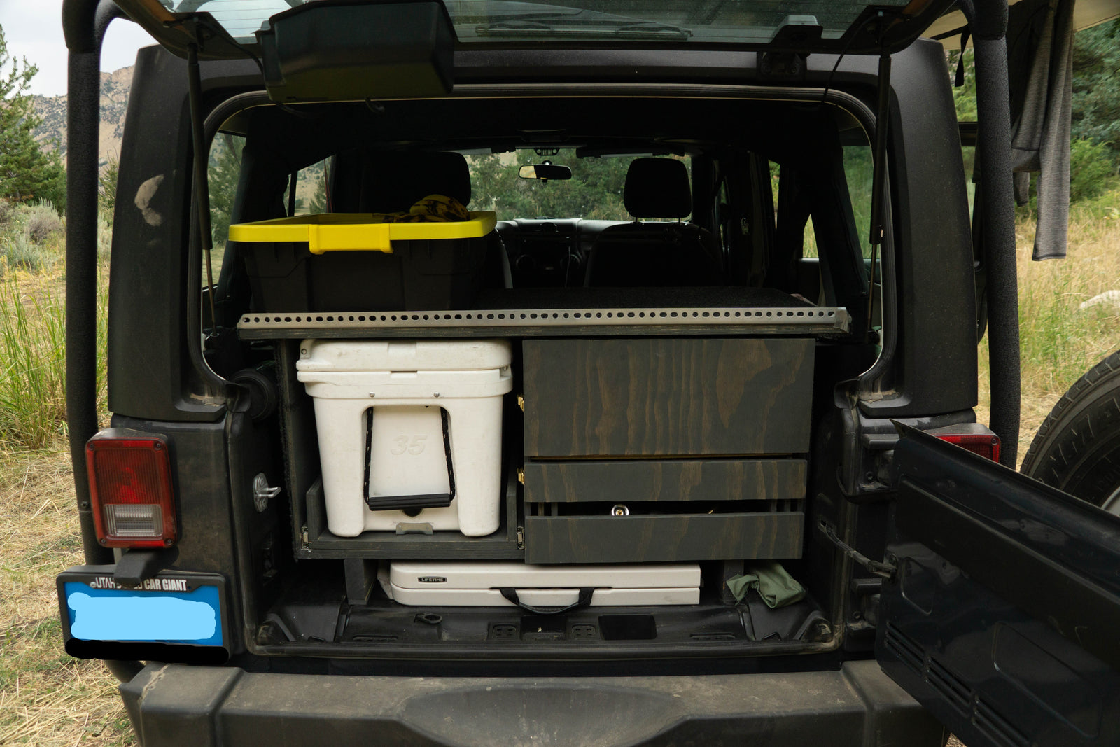 Rear of an SUV with custom camping storage: Yeti cooler, drawers, and bin. Ideal for RV rental adventures or overlanding.