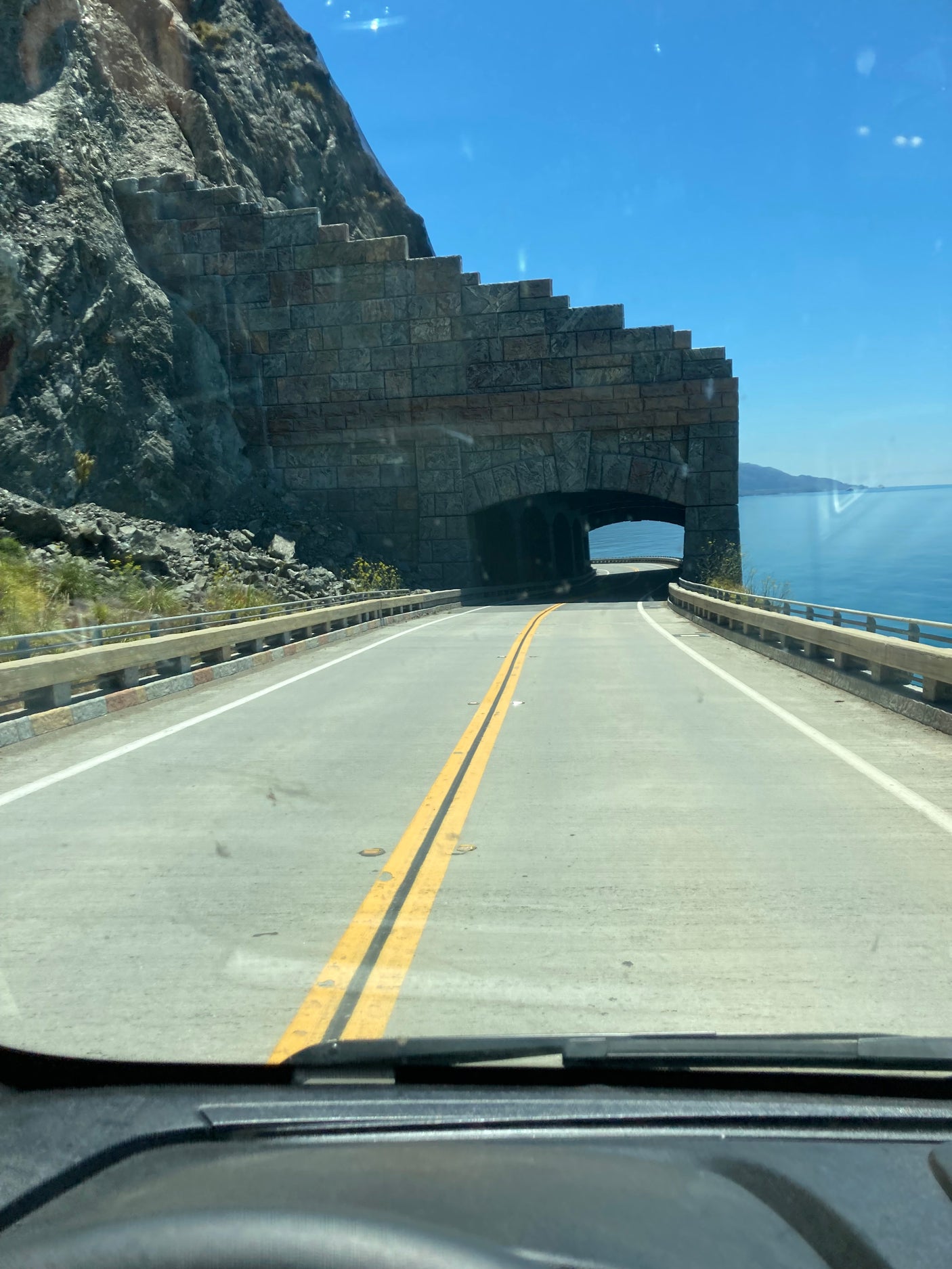 RV rental adventure: drive through a stone arch tunnel on a scenic coastal highway with ocean views and cliffs.