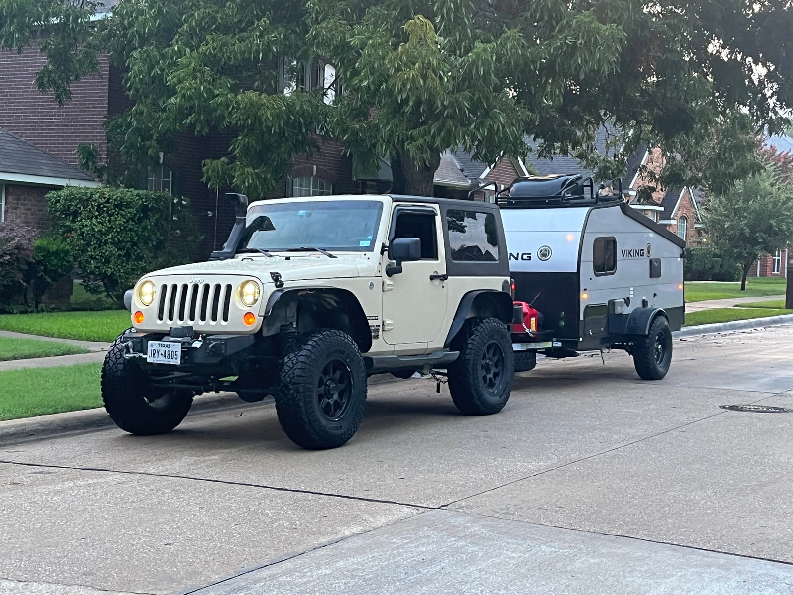 White Jeep Wrangler towing a gray Viking RV rental trailer on a suburban street, ready for adventure.