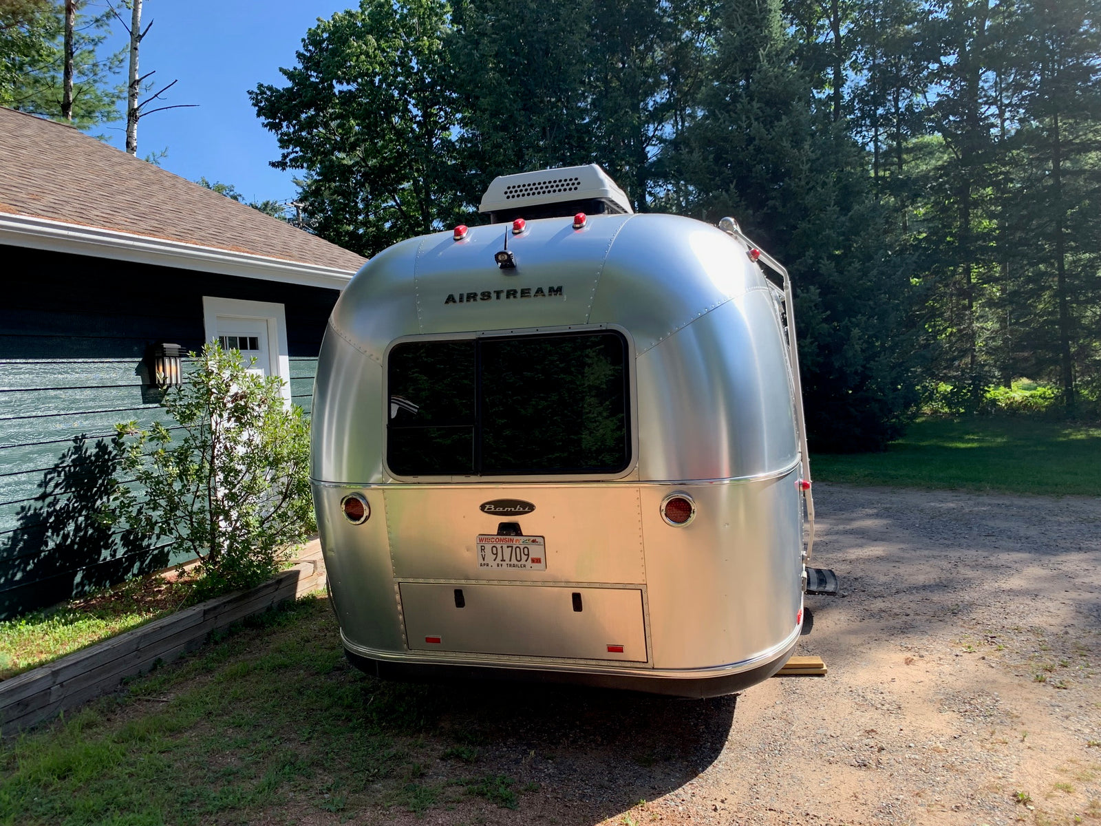 Airstream Bambi travel trailer, often available for rv rental, parked by a house amidst green trees.