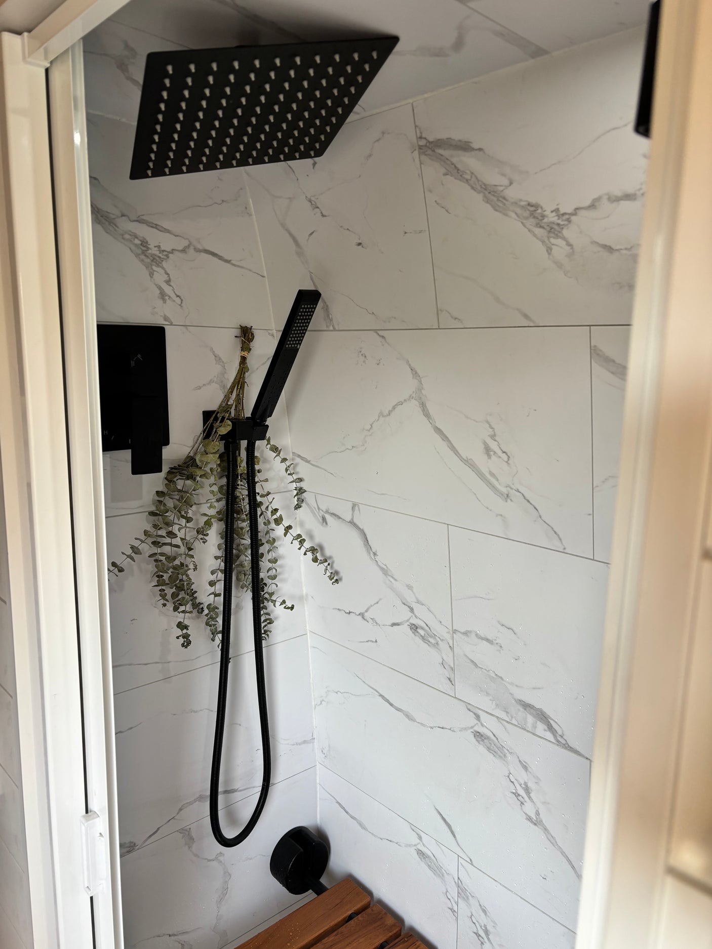 Modern RV rental shower: black fixtures, elegant marble-look tiles, and dried eucalyptus for a refreshing experience.