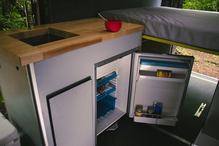 Step into this RV rental's practical kitchen area, complete with a sink, wood counter, and a fully accessible fridge.