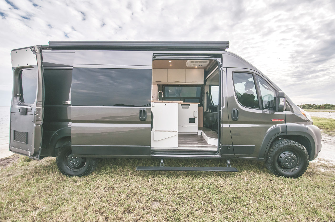 Grey camper van, side open revealing its custom interior, parked oceanside. Perfect for an rv rental adventure.