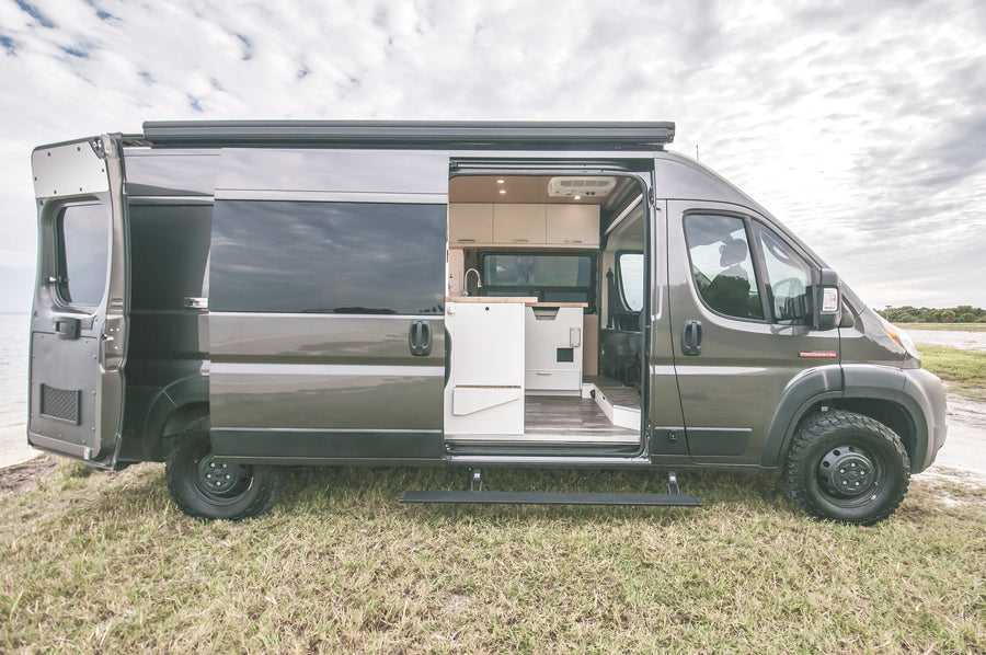 Grey camper van, side open revealing its custom interior, parked oceanside. Perfect for an rv rental adventure.