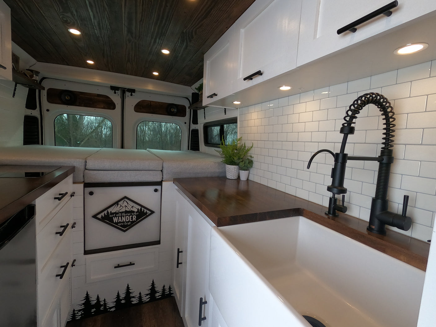 Inside a stylish RV rental camper van: white kitchen with a farm sink, wood counters, and gray bedding for a comfortable road trip.