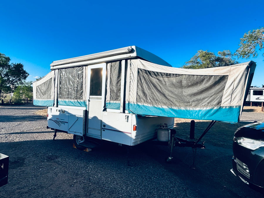 An RV rental, a pop-up camper, fully deployed under a clear blue sky at a gravel campsite. Ready for adventure.