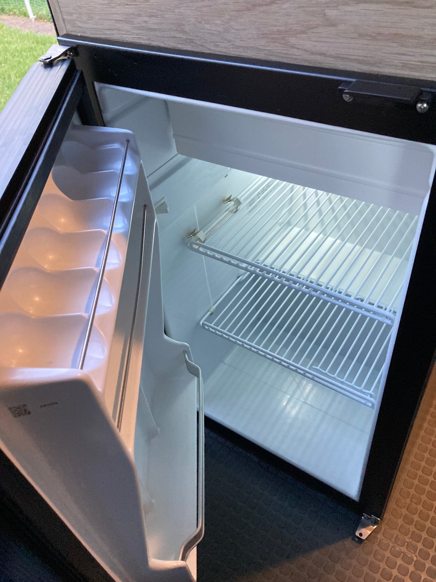 Inside an RV rental: An empty, open compact refrigerator with wire shelves, ready for travel provisions.