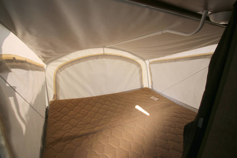 Cozy pop-up camper interior features a comfortable bed and built-in light, ideal for your next RV rental trip.