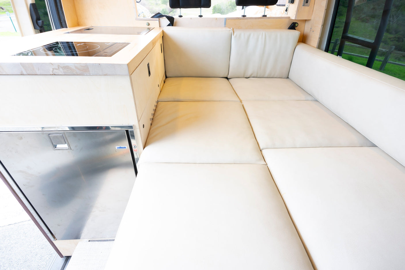 Comfortable RV rental interior: L-shaped seating, modern kitchenette with cooktop and built-in fridge.
