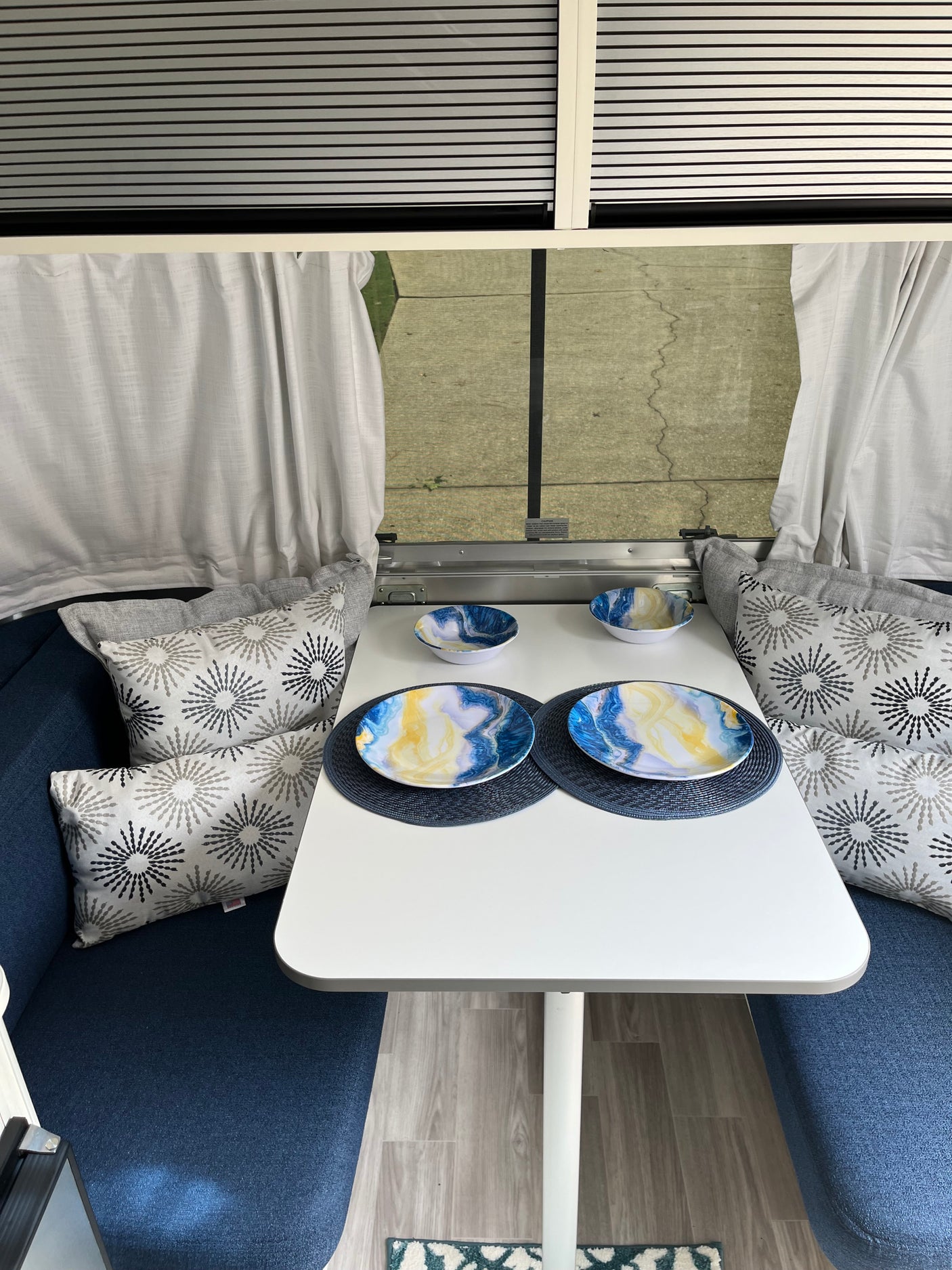 Inside an RV rental: a bright dinette area with blue seating, patterned pillows, a white table with colorful dishes.
